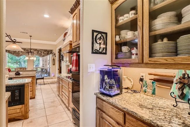 Kitchen featuring pendant lighting, ornamental molding, black microwave, light tile patterned floors, and light stone countertops | Image 14