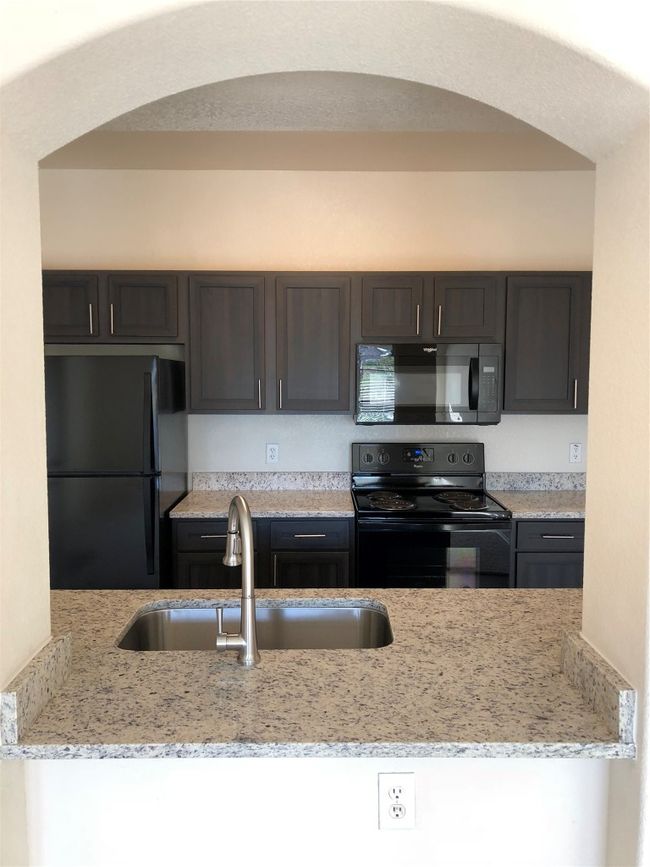 Kitchen with refrigerator, light stone counters, arched walkways, stove, and a sink | Image 8
