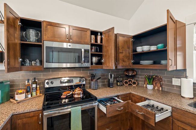 Kitchen with stainless steel appliances, open shelves, light stone counters, backsplash, and glass insert cabinets | Image 25