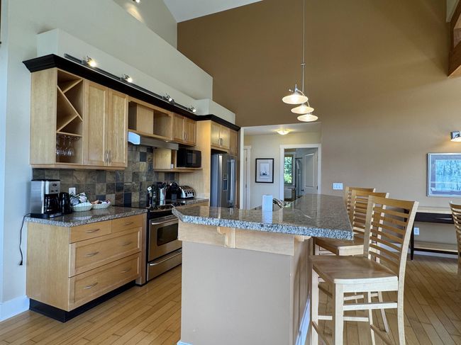 Kitchen with open shelves, stainless steel appliances, light brown cabinets, light wood-style floors, and a breakfast bar area | Image 7