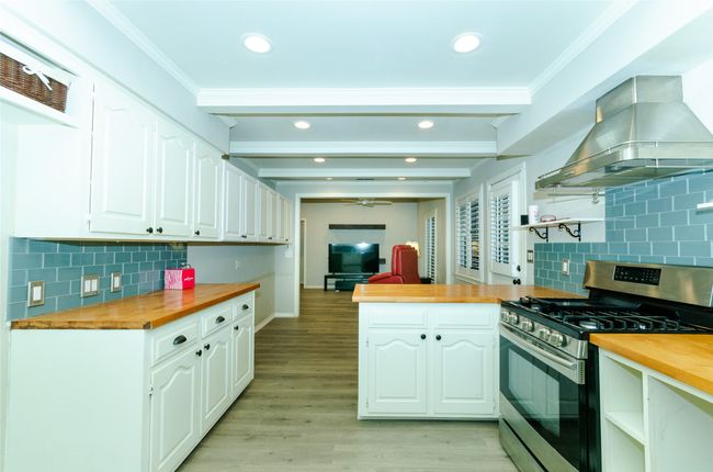 Kitchen featuring butcher block counters, backsplash, stainless steel gas range, a peninsula, and island exhaust hood | Image 8