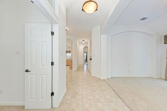 Hall with light tile patterned floors, arched walkways, light colored carpet, visible vents, and baseboards | Image 7