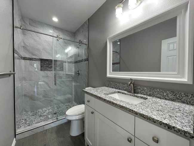 Master bathroom featuring granite top vanity, a stall shower, wood-look finished floors, and tasteful light fixtures | Image 19