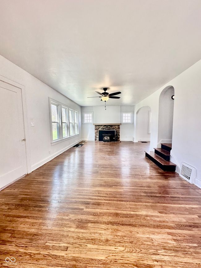 unfurnished living room with a fireplace, a ceiling fan, visible vents, arched walkways, and wood finished floors | Image 17