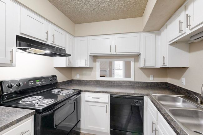Kitchen featuring dark countertops, under cabinet range hood, white cabinets, black appliances, and a sink | Image 20