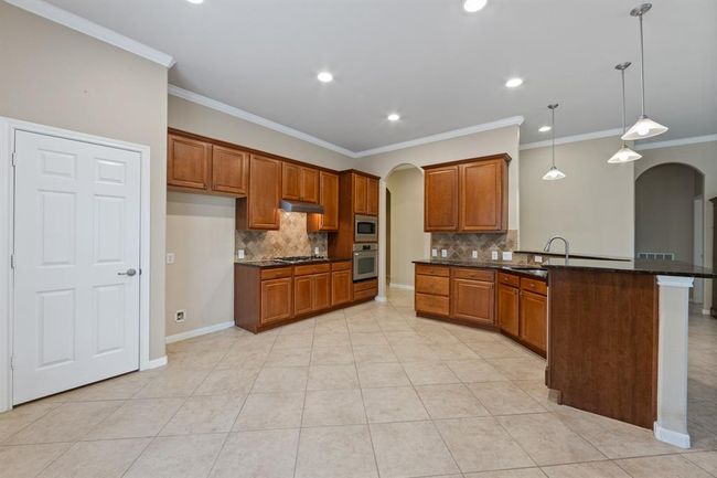 The kitchen offers plenty of storage with warm, wood-look cabinetry and stylish hanging light fixtures over the breakfast bar, creating a functional and inviting space for everyday living. | Image 23
