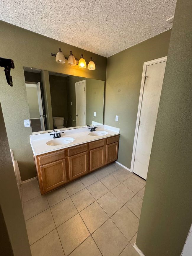 Bathroom featuring tile patterned floors, a textured ceiling, double vanity, and a textured wall | Image 12