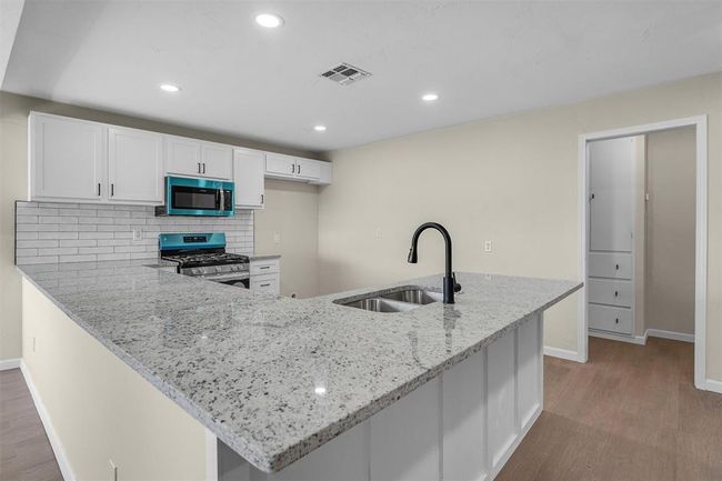 Kitchen with white cabinets, stainless steel appliances, light hardwood / wood-style floors, decorative backsplash, and sink | Image 20