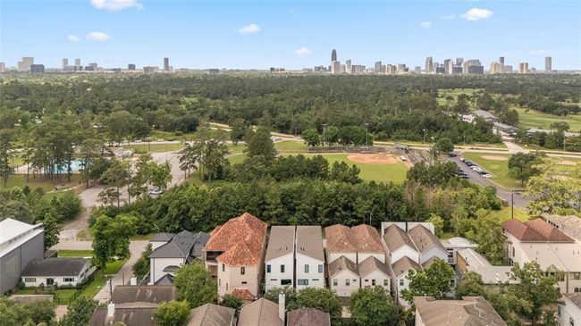 A stunning aerial view showcases a row of contemporary homes backing to lush, tree-filled parkland and ample green space just beyond. In the distance, the Houston skyline rises above the expansive Memorial Park, offering a rare blend of urban convenience and serene nature views. | Image 38
