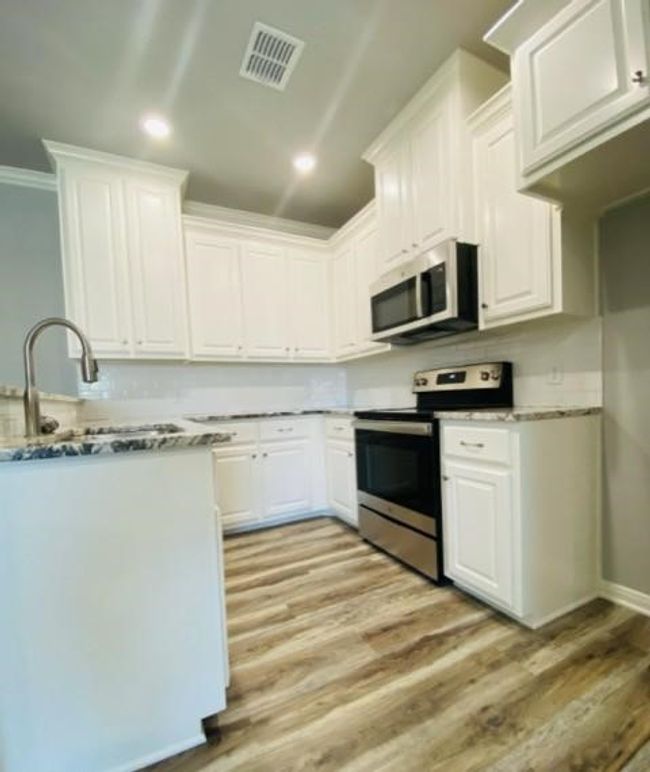 Kitchen featuring appliances with stainless steel finishes, white cabinets, light wood-style floors, ornamental molding, and a sink | Image 5