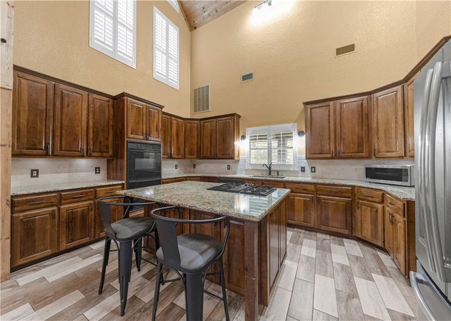 Kitchen featuring appliances with stainless steel finishes, high vaulted ceiling, decorative backsplash, a center island, and a textured wall | Image 12