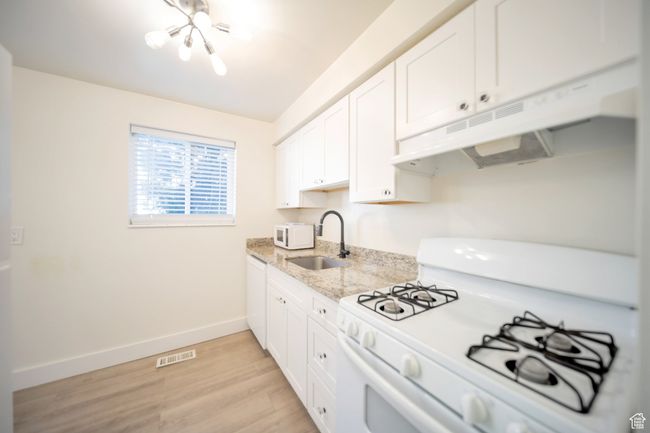 Kitchen with light stone countertops, white appliances, sink, light hardwood / wood-style floors, and white cabinetry | Image 4