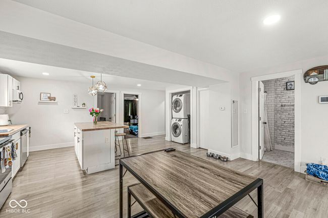 kitchen with stacked washer / drying machine, wooden counters, light wood-type flooring, baseboards, and a kitchen island | Image 10