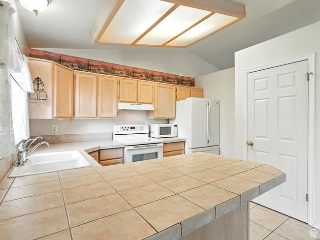 Kitchen with white appliances, light brown cabinetry, under cabinet range hood, vaulted ceiling, and a peninsula | Image 5