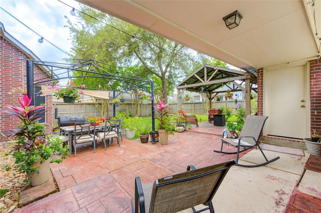 This inviting backyard features a spacious patio with comfortable seating and a dining area under a pergola. Surrounded by lush greenery and vibrant flowers, it's perfect for entertaining and relaxation. A cozy gazebo adds to the charm, providing shade and a peaceful retreat. | Image 33