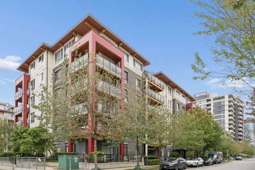 Modern multi-story building featuring a multi-toned facade, wood-finish eaves, glass-paneled balconies with black railings, and a street-level pedestrian walkway | Card Image