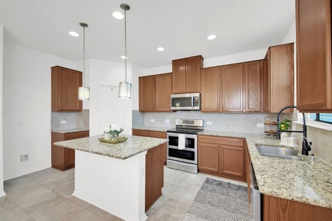 Kitchen with stainless steel appliances, a kitchen island, a sink, backsplash, and brown cabinetry | Image 18