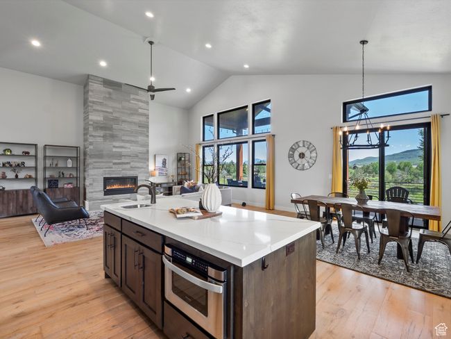 Kitchen with a tile fireplace, stainless steel oven, high vaulted ceiling, light wood-type flooring, and open floor plan | Image 13