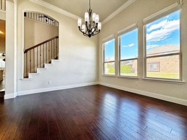 Empty room with a chandelier, crown molding, wood finished floors, and stairs | Image 5