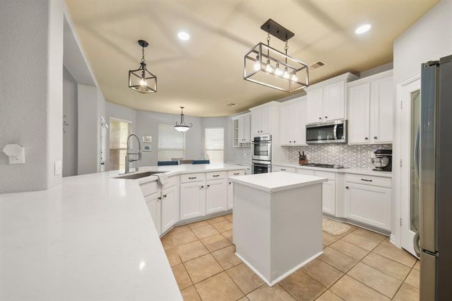 The kitchen with recessed lighting and tile flooring includes painted cabinets capped with crown & rope moulding along with updated quartz counter tops installed in 2021 and a tiled back splash. The center island with beautiful lighting above (installed in 2024) provides additional prep space with storage below. | Image 15