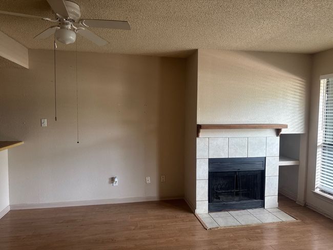 Unfurnished living room featuring a textured ceiling, a fireplace, wood finished floors, a ceiling fan, and a textured wall | Image 6
