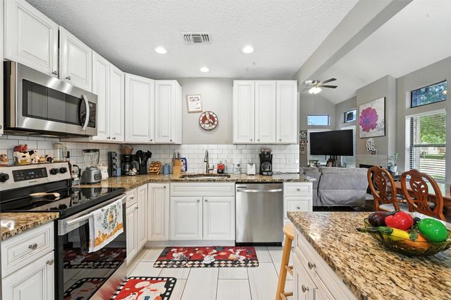 Kitchen with appliances with stainless steel finishes, backsplash, ceiling fan, light tile patterned floors, and white cabinets | Image 9