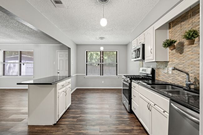 Kitchen with appliances with stainless steel finishes, a sink, dark countertops, a textured ceiling, and dark wood finished floors | Image 4