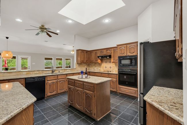 Kitchen featuring under cabinet range hood, a ceiling fan, decorative backsplash, and black appliances | Image 10