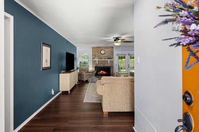 Living area featuring a brick fireplace, dark wood-style floors, ornamental molding, a ceiling fan, and baseboards | Image 6