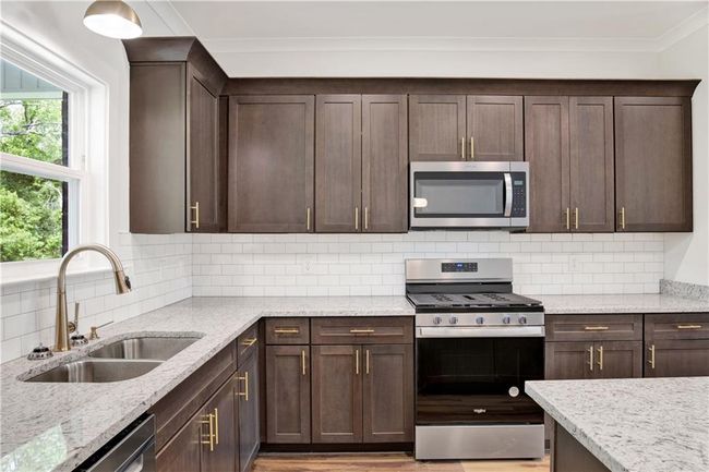 Kitchen featuring dark brown cabinets, light stone counters, a sink, stainless steel appliances, and ornamental molding | Image 15