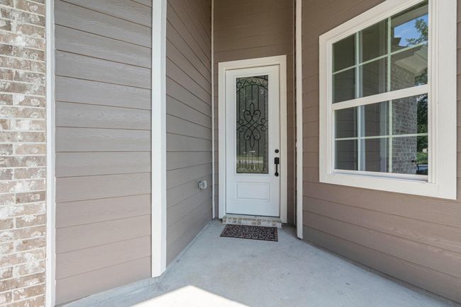 This photo shows a welcoming front entryway with a decorative glass door and adjacent window, framed by light brown siding and brick accents. | Image 32