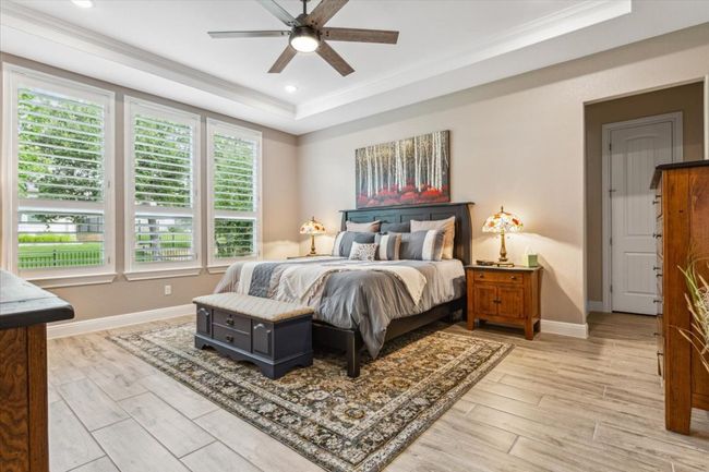 Bedroom featuring crown molding, light wood look tile flooring, a raised ceiling, and a ceiling fan | Image 18