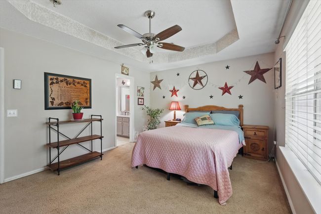 Bedroom featuring a raised ceiling, a ceiling fan, baseboards, light colored carpet, and ensuite bathroom | Image 21