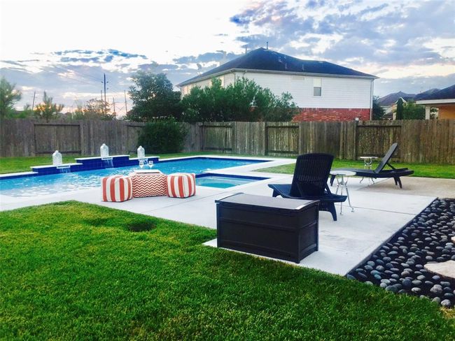 This photo showcases a spacious backyard featuring a well-maintained pool with water features. It includes a surrounding patio area with lounge chairs and a seating area, offering a perfect space for relaxation and outdoor entertaining. The yard is enclosed by a wooden fence, providing privacy. | Image 7
