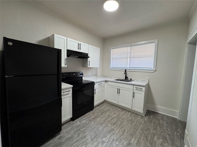 Kitchen with a sink, under cabinet range hood, black appliances, ornamental molding, and white cabinets | Image 6