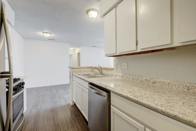 Kitchen featuring stainless steel appliances, a sink, dark wood finished floors, white cabinets, and a textured ceiling | Image 10