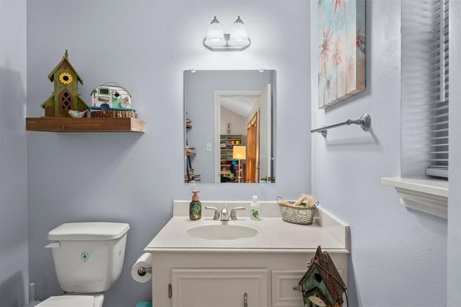 This bathroom features a clean, modern design with light-colored walls and a vanity with ample counter space. It includes a mounted mirror, decorative shelving, and a window for natural light. | Image 15