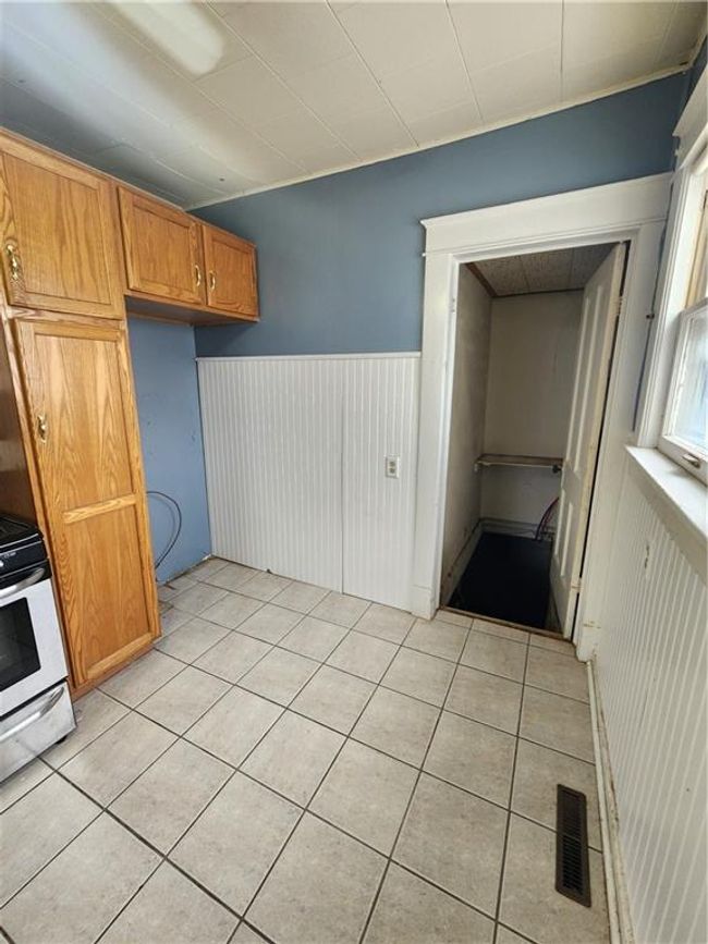 Kitchen with light tile patterned flooring, wainscoting, brown cabinetry, stove, and visible vents | Image 22