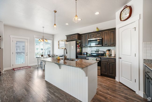 Kitchen featuring appliances with stainless steel finishes, a breakfast bar, dark wood-type flooring, backsplash, and recessed lighting | Image 6