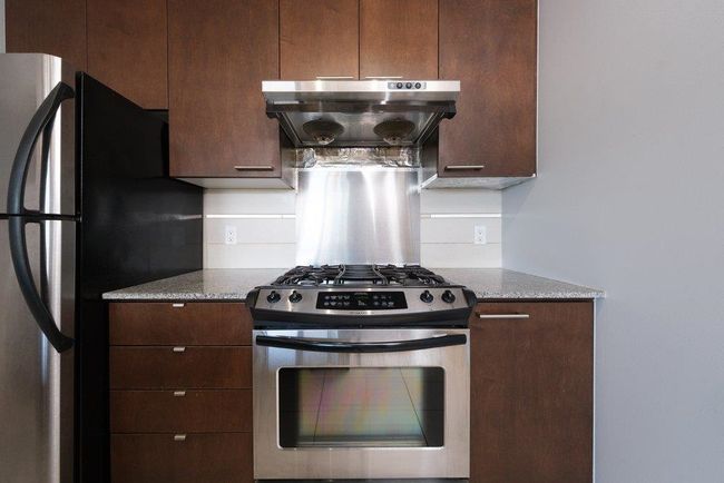 Kitchen with dark brown cabinets, light stone counters, under cabinet range hood, and stainless steel appliances | Image 5