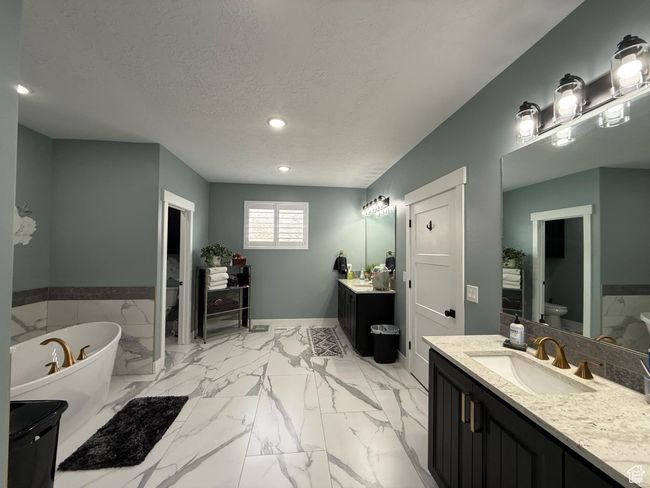 Full bathroom featuring a textured ceiling, toilet, a freestanding tub, two vanities, and a sink | Image 40