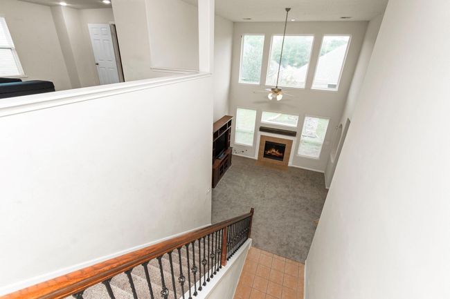 This photo showcases a spacious, two-story living area with large windows, providing ample natural light. The room features a cozy fireplace and an open view from the upper level, complemented by a wooden staircase with iron railings. | Image 29