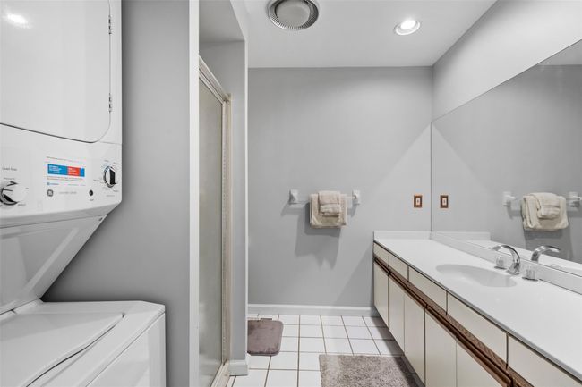 Full bathroom with a shower stall, vanity, tile patterned floors, baseboards, and stacked washer and dryer | Image 12