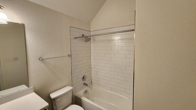 Full bathroom with a textured wall, toilet, lofted ceiling, and shower / bath combination | Image 13