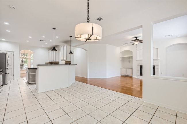 Kitchen with arched walkways, a ceiling fan, a tiled fireplace, dark countertops, and freestanding refrigerator | Image 13