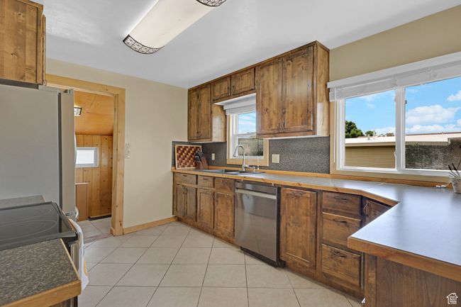 Kitchen with stainless steel appliances, a sink, backsplash, light tile patterned floors, and brown cabinets | Image 12