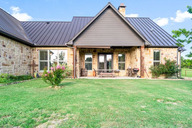 Back of property with a standing seam roof, a metal roof, a chimney, stone siding, and a yard | Image 34