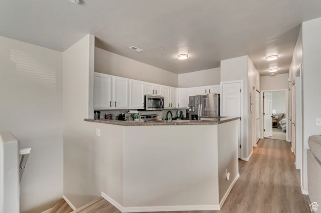 Kitchen featuring light wood-style floors, stainless steel appliances, a peninsula, and white cabinetry | Image 7