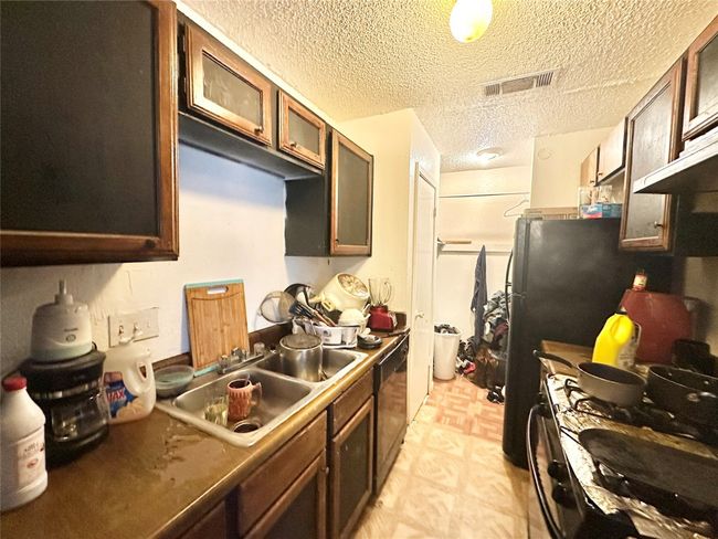 Kitchen with gas range gas stove, a sink, light flooring, black dishwasher, and glass insert cabinets | Image 9