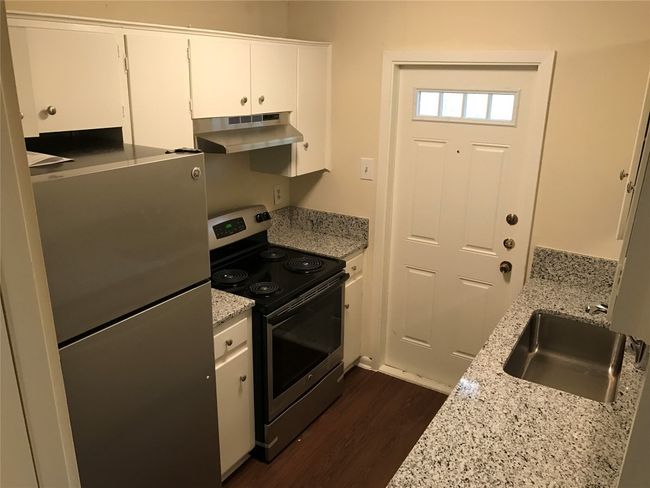 Kitchen with stainless steel appliances, under cabinet range hood, white cabinetry, a sink, and dark wood-style floors | Image 4